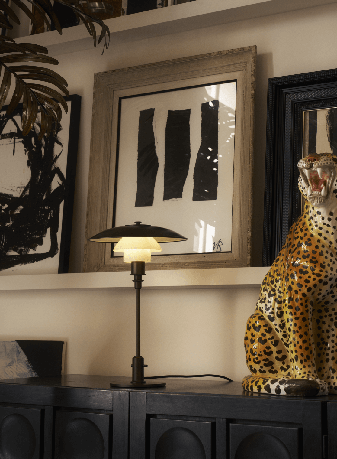  Table lamp on dark cabinet beside bold artwork and ceramic leopard, © 2025 Louis Poulsen.