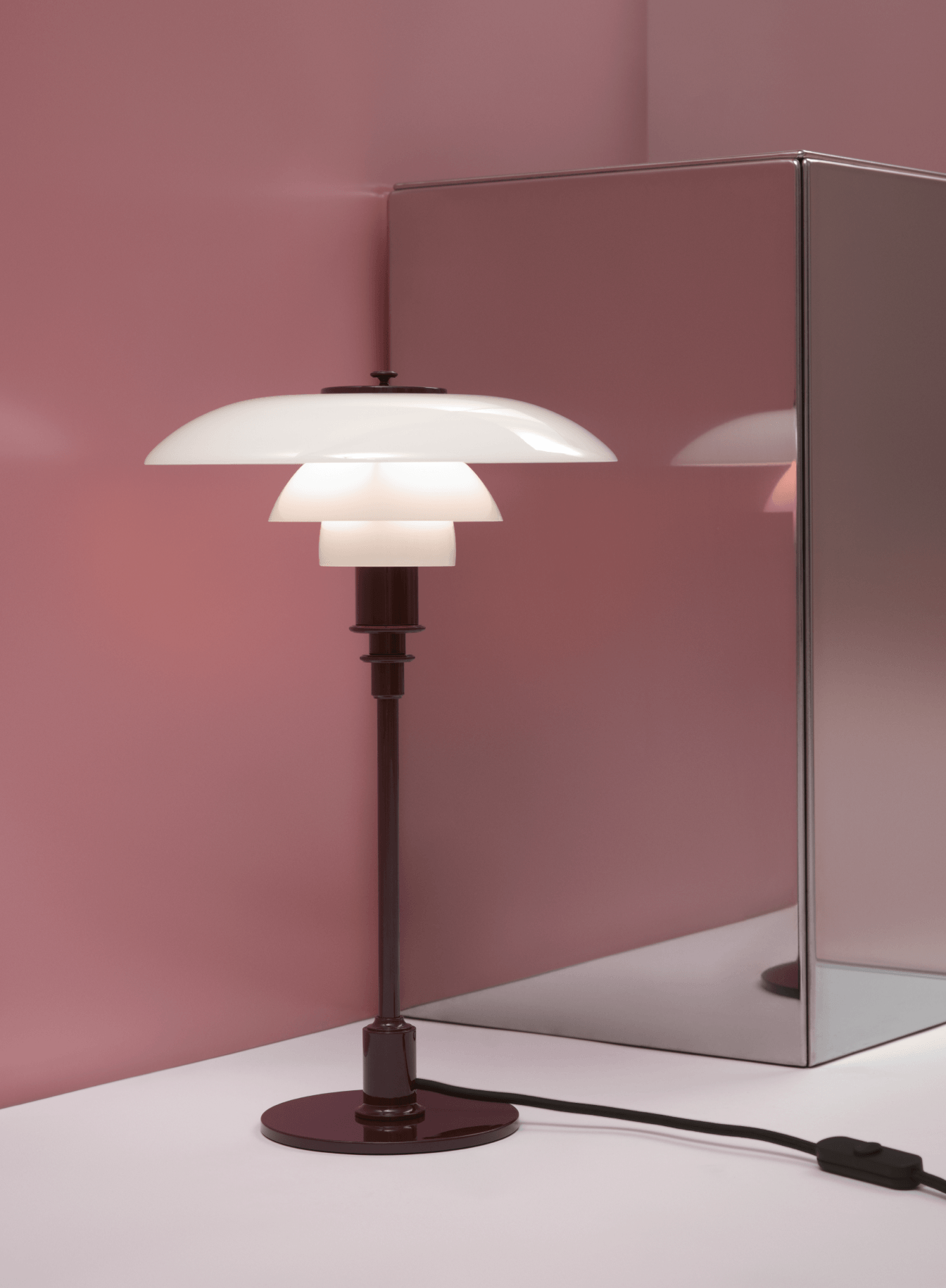 PH 3/2 Tischleuchte in Glossy Burgundy mit leuchtenden Opalglasschirmen neben einem verspiegelten Podest, © 2025 Louis Poulsen.