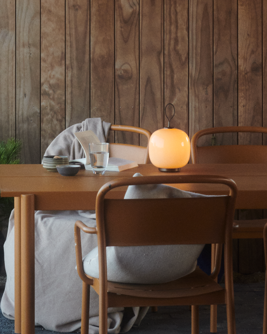 VL45 Portable lamp glowing on outdoor dining table with wooden wall backdrop, © 2025 Louis Poulsen.