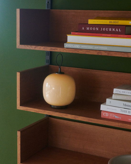 VL45 Portable lamp on wooden bookshelf beside stacked books, © 2025 Louis Poulsen.