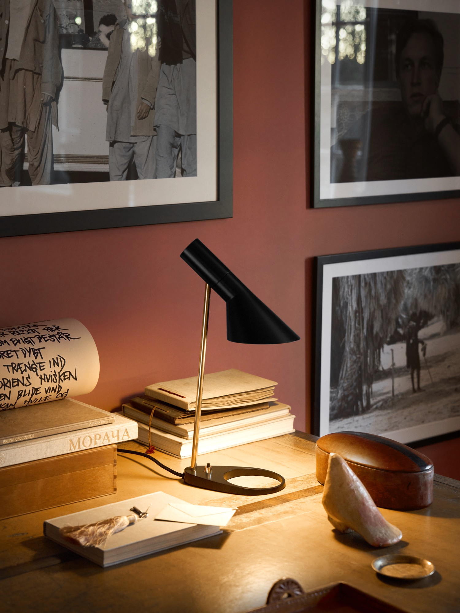 AJ table lamp illuminating wooden desk with art, © 2025 Louis Poulsen.