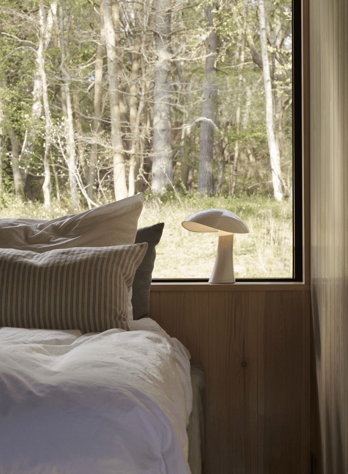 Rumee portable lamp placed on a windowsill, illuminating the interior of a serene bedroom, © 2025 Louis Poulsen.