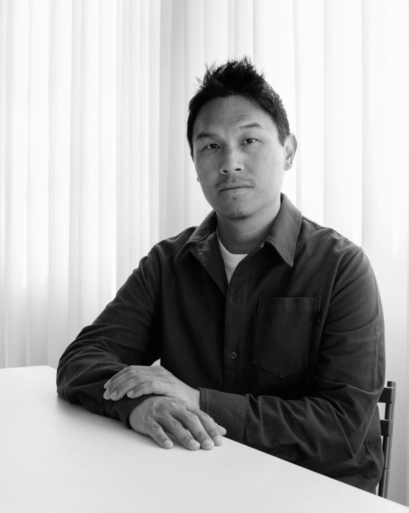 Porträt des Designers Gabriel Tan am Tisch vor weichem Vorhang, © 2025 Louis Poulsen.