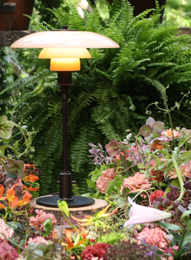 PH 3/2 Limited Edition Table Lamp glowing among vibrant flowers and ferns, © 2025 Louis Poulsen.
