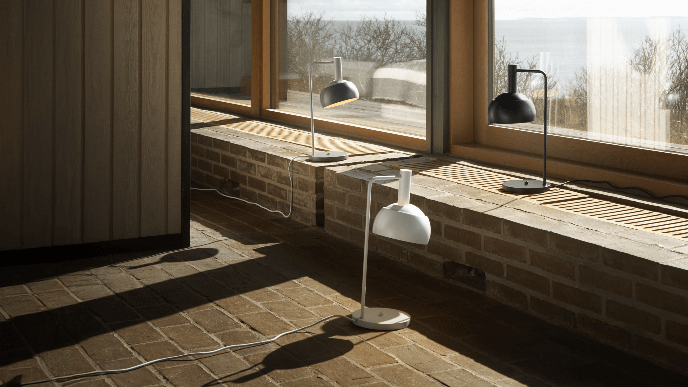 FJ Element Table Lamps in White, Grey and Black placed by window with sea view, © 2025 Louis Poulsen.