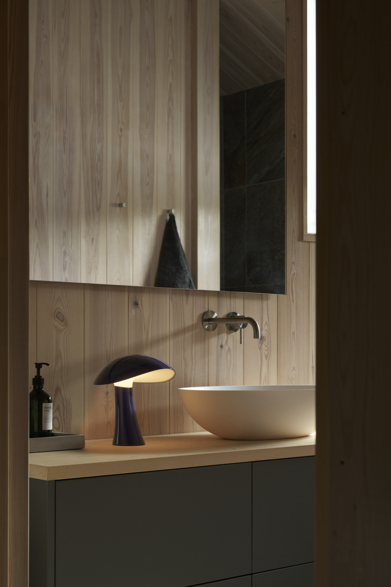 Rumee Portable in blue on wooden bathroom counter, © 2025 Louis Poulsen.