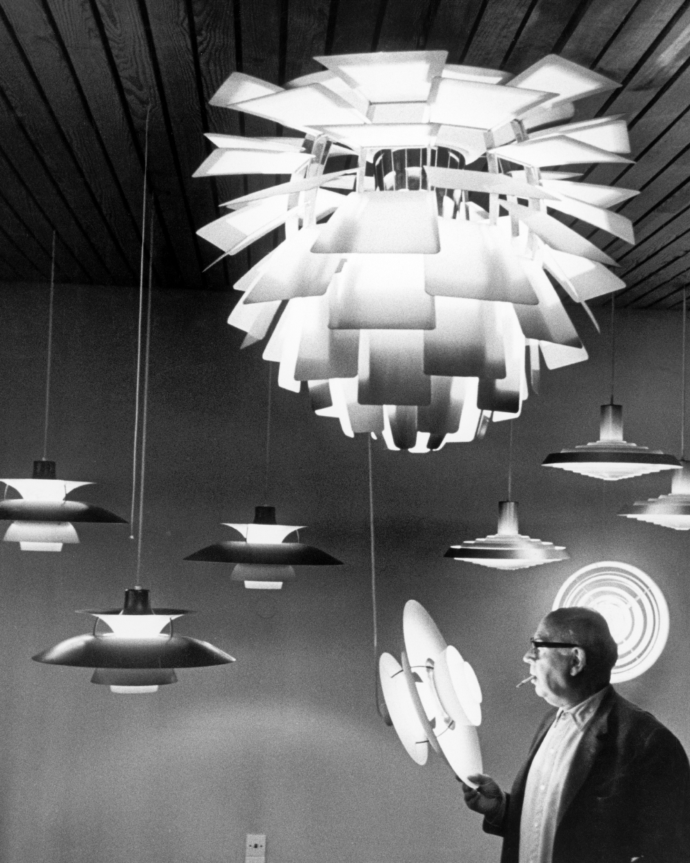 Poul Henningsen observing Artichoke and PH lamps hanging in showroom, © 2025 Louis Poulsen.